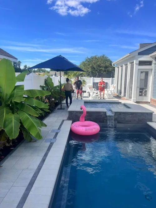 4 after Compact Pool and Spa Construction - Solid Structures Backyard Pool Scene with a Pink Flamingo Float in the Water and People Gathered by a Blue Umbrella and Seating Area.