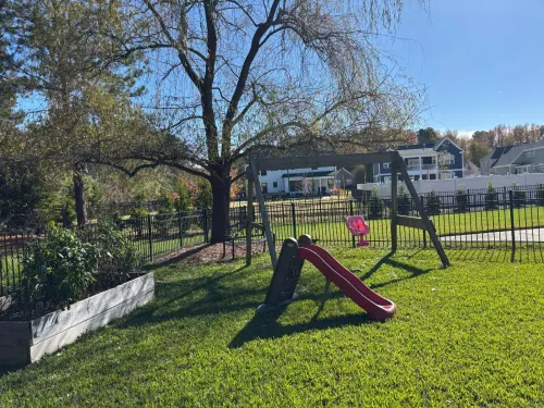 4 before Backyard Transformation with Pool and Outdoor Living in Great Bridge - Solid Structures Backyard Playground with a Red Curved Slide and Swings, Fenced Lawn, and Trees with Houses in the Distance.
