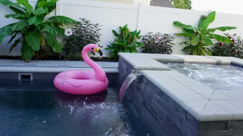 8 after Compact Pool and Spa Construction - Solid Structures Pink Flamingo Pool Float in a Blue Pool, with Tropical Plants and a White Fence in the Background.
