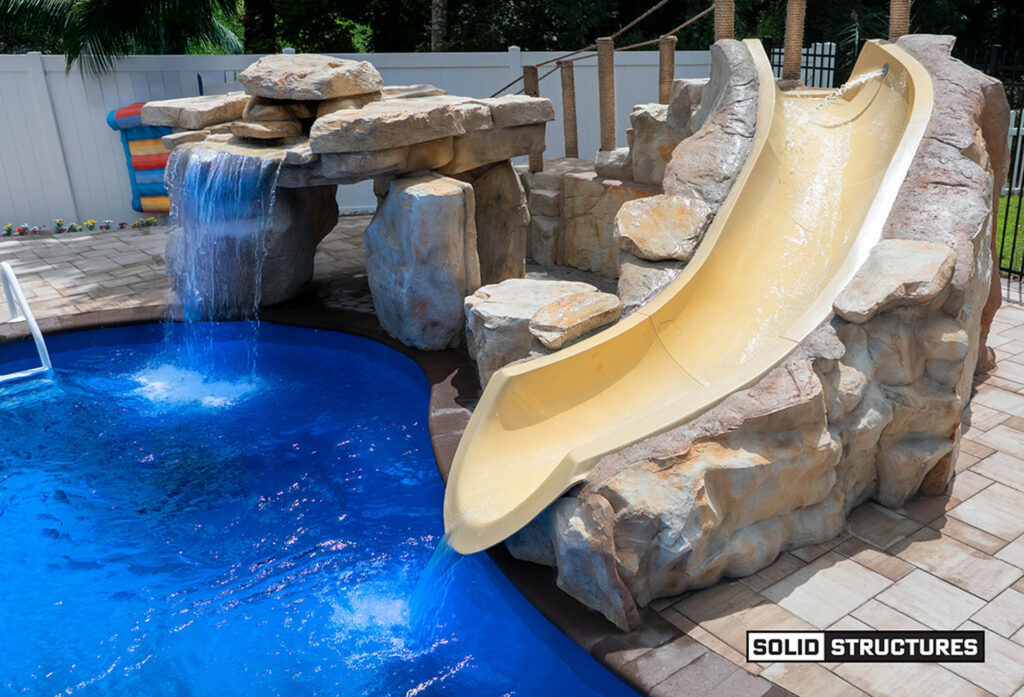 Ricorock, Grotto and Water Slide: Sr Smith Bigride Water Slide Right Turn 5.5 Feet-taupe-br-2l-tp with Pkg 15 From, Paver Walkway: Belgard 2'x3' Slabs Color: Sandbridge, Coping: Belgard Marina Coping Color: Chocolate, Fence:6' Tall Black Aluminum Fence with Through Pickets, Rockbed: 1-3" Brown/white/tan River Rock with Landscaping Fabric Beneath, 6' Tall White Vinyl Privacy Fence with a 10' Wide Gate (two 5' Gate Leaves Each) and a 5' Wide Gate, Pavers: Belgard Dimensions 12 Color: Sandbridge Standard Finish with Chocolate 6x9 Accent Stones in Soldier Course, Pool: Thursday Pools 36' Wellspring Color: Maya