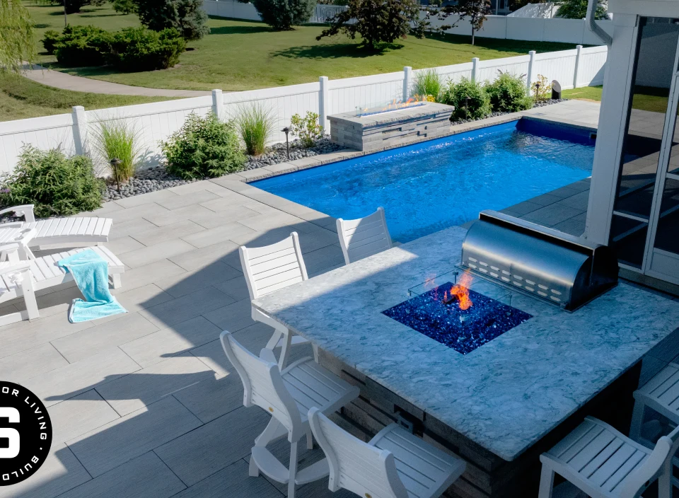 Modern backyard with a rectangular blue pool, white patio furniture, and a built-in fire pit table.